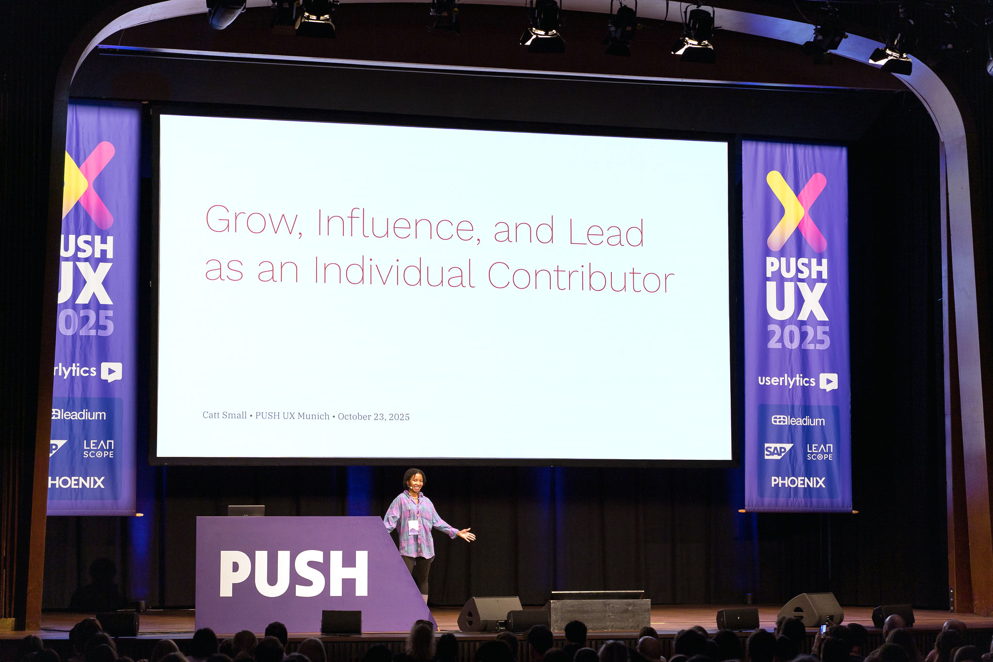 Catt Small speaking onstage at PUSH UX 2025 beneath a slide about influence and individual-contributor leadership.
